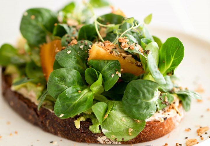 a white plate topped with a piece of bread covered in veggies